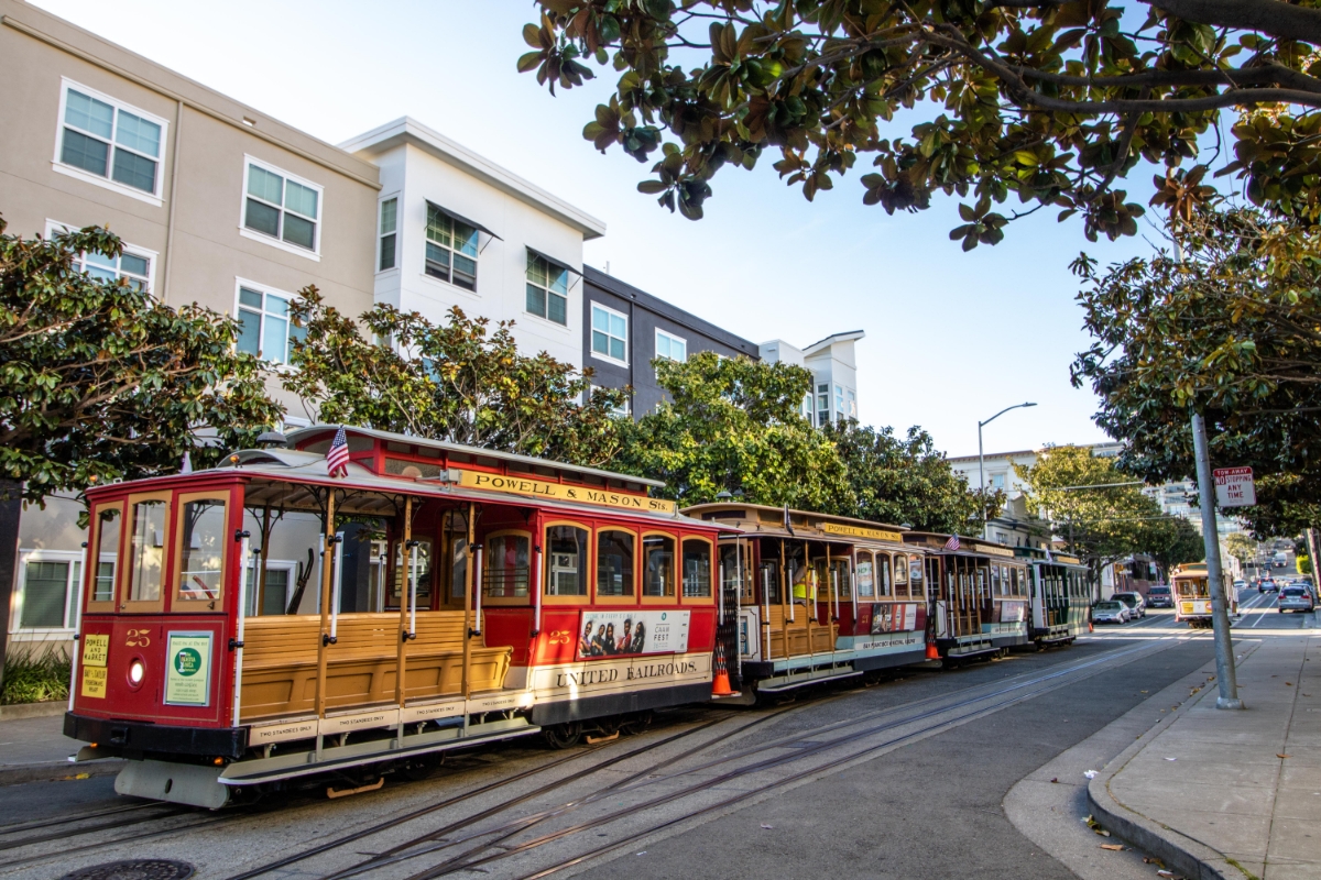 Traditional red cable car on Powell and Mason Street line with modern city buildings in background