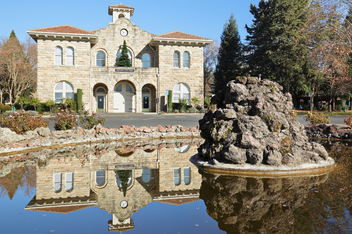 Stone City Hall building perfectly reflected in plaza duck pond with decorative rock formation