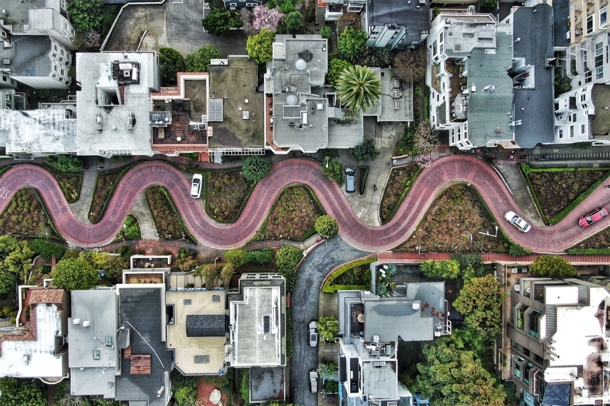 Aerial and street-level views of Lombard Street in San Francisco showing its famous zigzag brick path, flower gardens, surrounding homes, and Bay vista in perfect sunny weather conditions.