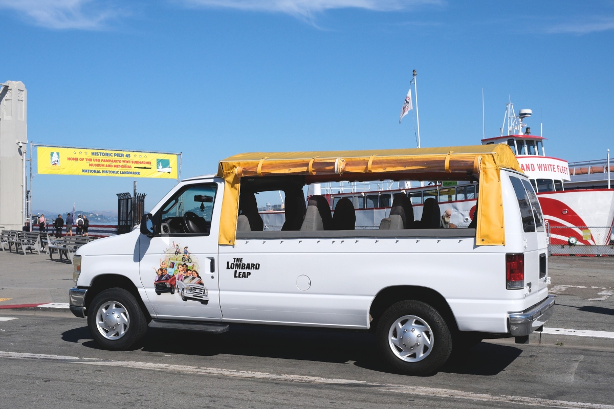 White tour van labeled 'The Lombard Leap' parked at Fisherman's Wharf near Historic Pier 43 and Red and White Fleet