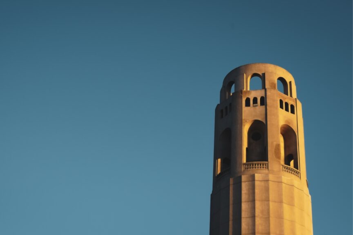 Close-up of Coit Tower's distinctive Art Deco crown and observation deck bathed in warm sunset light against deep blue sky