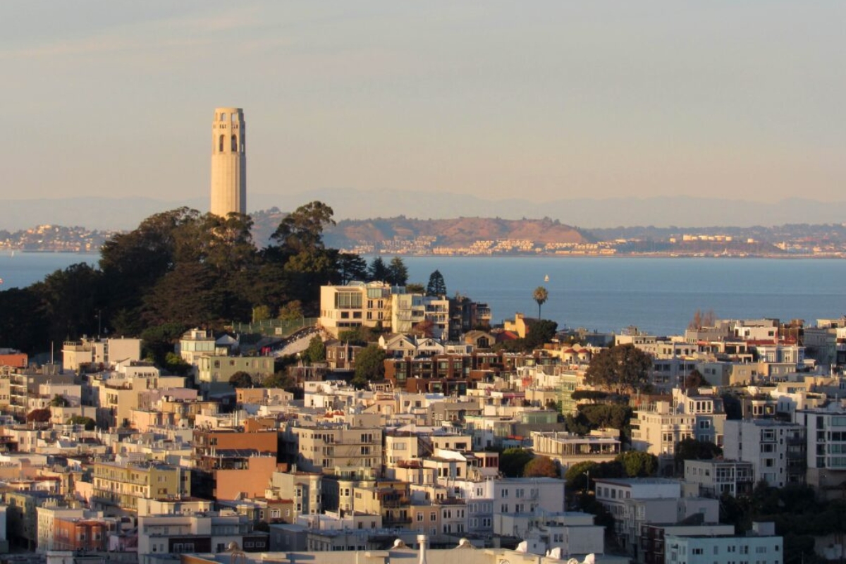 Coit Tower atop Telegraph Hill in San Francisco with panoramic views of the bay, residential buildings, and city skyline in warm sunset light