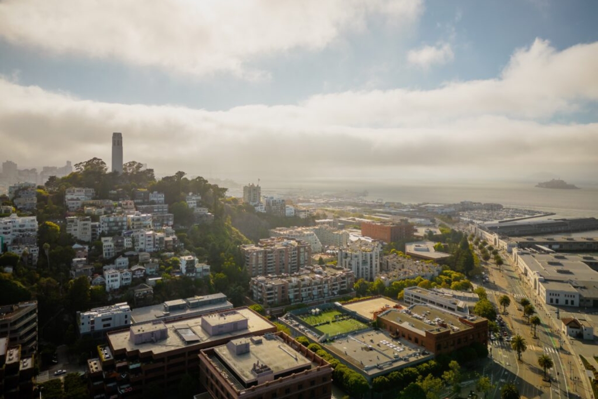 Atmospheric view of San Francisco morning fog rolling across the Bay with Coit Tower on Telegraph Hill, waterfront, and city neighborhoods in golden sunlight